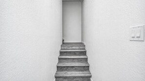Un escalier étroit aux murs blancs mène à une porte située en haut.