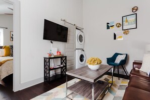 A modern living room with a flat-screen TV mounted on the wall, a washing machine, a coffee table with a bowl of popcorn, a blue chair, and a brown leather sofa. - MODERN & LUXURY STAY in Austin, Mins to Downtown! (Austin)