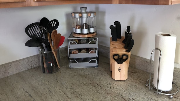 Una encimera de cocina con armarios de madera, un organizador de especias, una cafetera, un juego de cuchillos y un dispensador de toallas de papel.