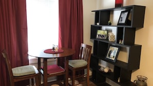 Un comedor con una mesa redonda, dos sillas, una estantería y una ventana con cortinas.