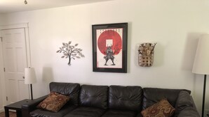 Una sala de estar con un sofá de cuero oscuro, dos platos decorativos rojos sobre una mesa de centro negra, una obra de arte enmarcada con un círculo rojo, un adorno montado en la pared y una lámpara.