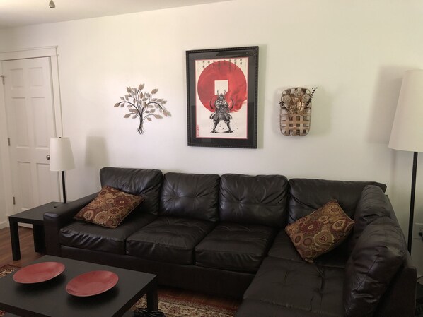 A living room with a dark leather sofa, two red decorative plates on a black coffee table, a framed artwork with a red circle, a wall-mounted decorative piece, and a lamp.