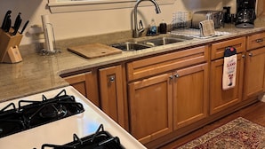 Una cocina con armarios de madera, una estufa a gas, un fregadero y un ventanal con persianas.