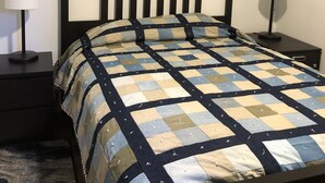 Una cama bien tendida con colcha, un cuadro enmarcado encima y dos mesitas de noche con lámparas.