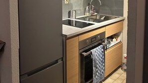 A compact kitchen with wooden cabinets, a stainless steel refrigerator, a built-in oven, and a sink with a modern faucet. - Maison au Calme à Proximité du lac (Hourtin)