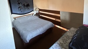 A small, compact room with a bed, a bench, and a suitcase. - Maison au Calme à Proximité du lac (Hourtin)