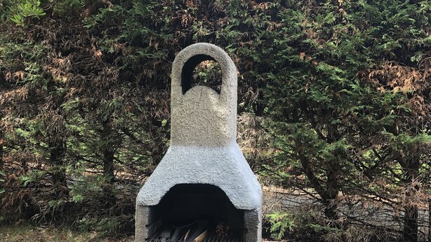 A stone-built outdoor grill with a firebox, surrounded by gravel and dense foliage. - Maison au Calme à Proximité du lac (Hourtin)