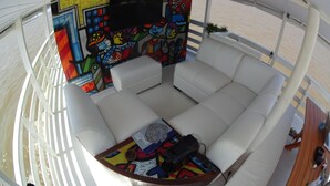 A white boat interior with a colorful mural on one wall, a cushioned seating area, and a small table with a book and a camera. - Gorgeous converted fishing vessel in Alter do Chao (Alter do Chao)