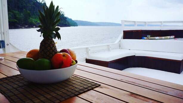 A wooden table with a bowl of fruit and a white cushioned bench on a boat deck. - Gorgeous converted fishing vessel in Alter do Chao (Alter do Chao)