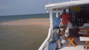 A beachside restaurant with a view of the ocean, outdoor seating, and a water dispenser. - Gorgeous converted fishing vessel in Alter do Chao (Alter do Chao)