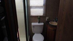 A small bathroom with a toilet, a sink, and a window with blinds. - Cozy Camper/RV: Hot tub available  (Bastrop)