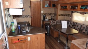 A compact RV kitchen with wooden cabinetry, a sink, a coffee maker, and a small table. - Cozy Camper/RV: Hot tub available  (Bastrop)