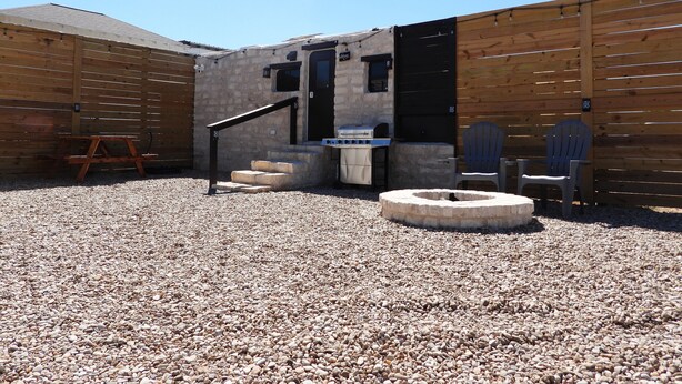 A patio area with a grill, a wooden chair, and a stone seating area. - Cozy Camper/RV: Hot tub available  (Bastrop)