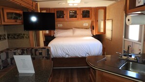 A compact RV interior with a bed, kitchenette, and a mounted TV. - Cozy Camper/RV: Hot tub available  (Bastrop)