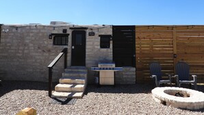 A rustic outdoor area with a stone wall, a wooden door, a barbecue grill, and a fire pit. - Cozy Camper/RV: Hot tub available  (Bastrop)