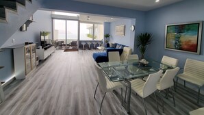 Ein modernes Wohnzimmer mit einem Glastisch, weißen Stühlen, einem blauen Sofa und einer Treppe.