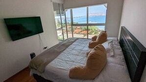 Ein Schlafzimmer mit einem Bett, einem an der Wand montierten Fernseher und einem großen Fenster mit Blick auf das Meer und die Landschaft.