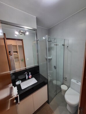 Une salle de bain moderne avec une douche à parois de verre, des toilettes blanches et un plan de toilette noir doté d’un lavabo et d’un distributeur de savon.