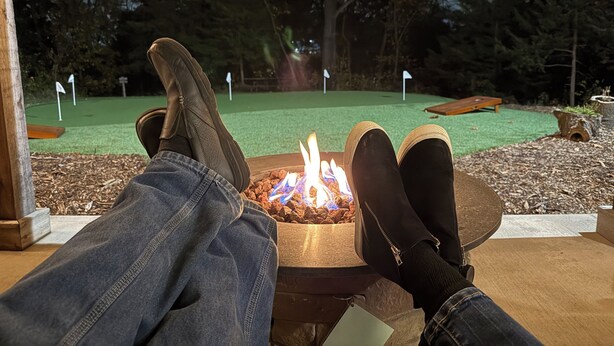 A person relaxing with legs propped up on a table, overlooking a miniature golf course at night. - Two Bedroom Relaxing Woodland Getaway with Putting Green and Walking Trails (Edwardsville)