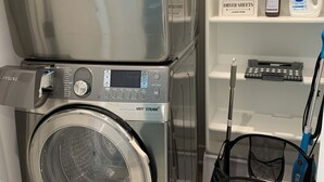 A laundry room with two stacked front-loading washing machines, a shelf with cleaning supplies, and a mop. - Two Bedroom Relaxing Woodland Getaway with Putting Green and Walking Trails (Edwardsville)