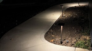 A curved concrete pathway with a light source on the right, surrounded by soil and vegetation. - Two Bedroom Relaxing Woodland Getaway with Putting Green and Walking Trails (Edwardsville)