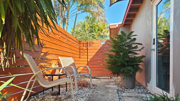 A patio area with a wooden fence, two metal chairs, a small table, and a potted plant. - Queen. Minutes to Wilton drive. Private entrance and bathroom (Wilton Manors)