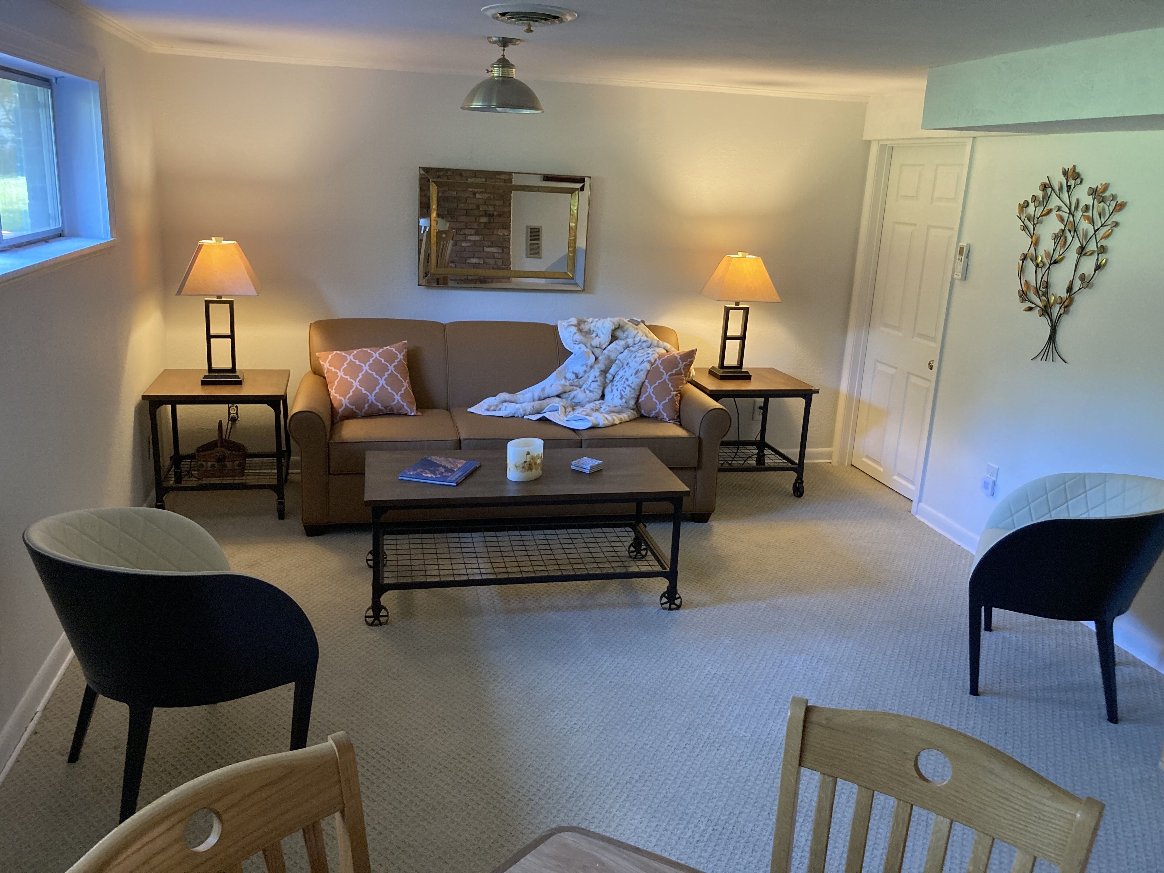 A cozy living room with a sofa, two side tables with lamps, a coffee table, and two chairs.