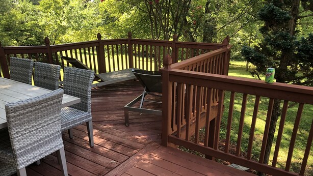 A wooden deck with wicker chairs and a table, surrounded by a wooden railing and greenery. - Visit Monticello, Wineries, UVA:  Room for a Crowd (Troy)