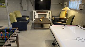 A room with a pool table, two sofas, a television, and a foosball table.