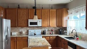 A kitchen with wooden cabinets, a central island, a sink, and a stove. - 3 bedroom house 5 minutes away from the airport in Colorado Springs all for you. (Colorado Springs)