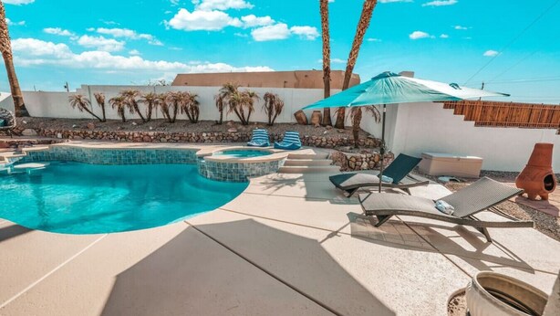 Una piscina con hidromasaje, sillas de descanso y una pérgola con sombrilla azul.