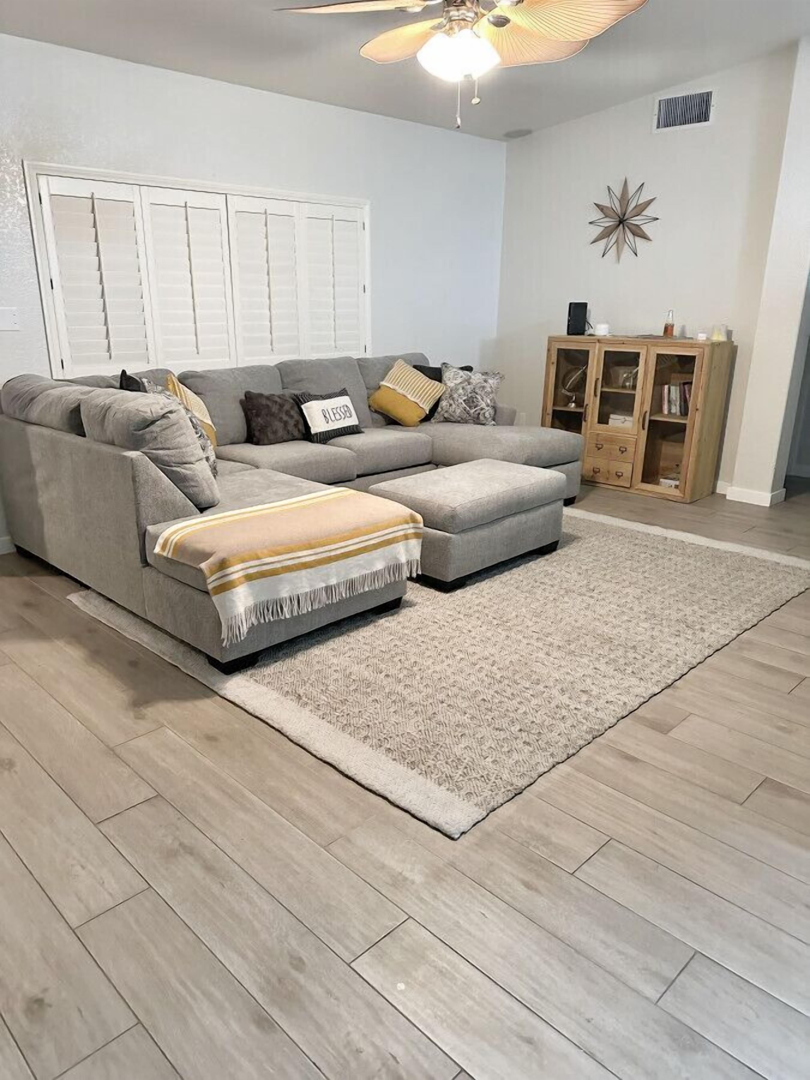 A living room with a grey sectional sofa, a beige rug, and a wooden cabinet.