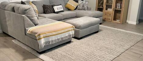 A living room with a grey sectional sofa, a beige rug, and a wooden cabinet.