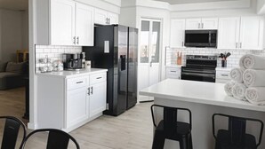 Una cocina moderna con armarios blancos, un refrigerador negro, un microondas y una estufa. Hay taburetes de bar y una mesa de comedor.