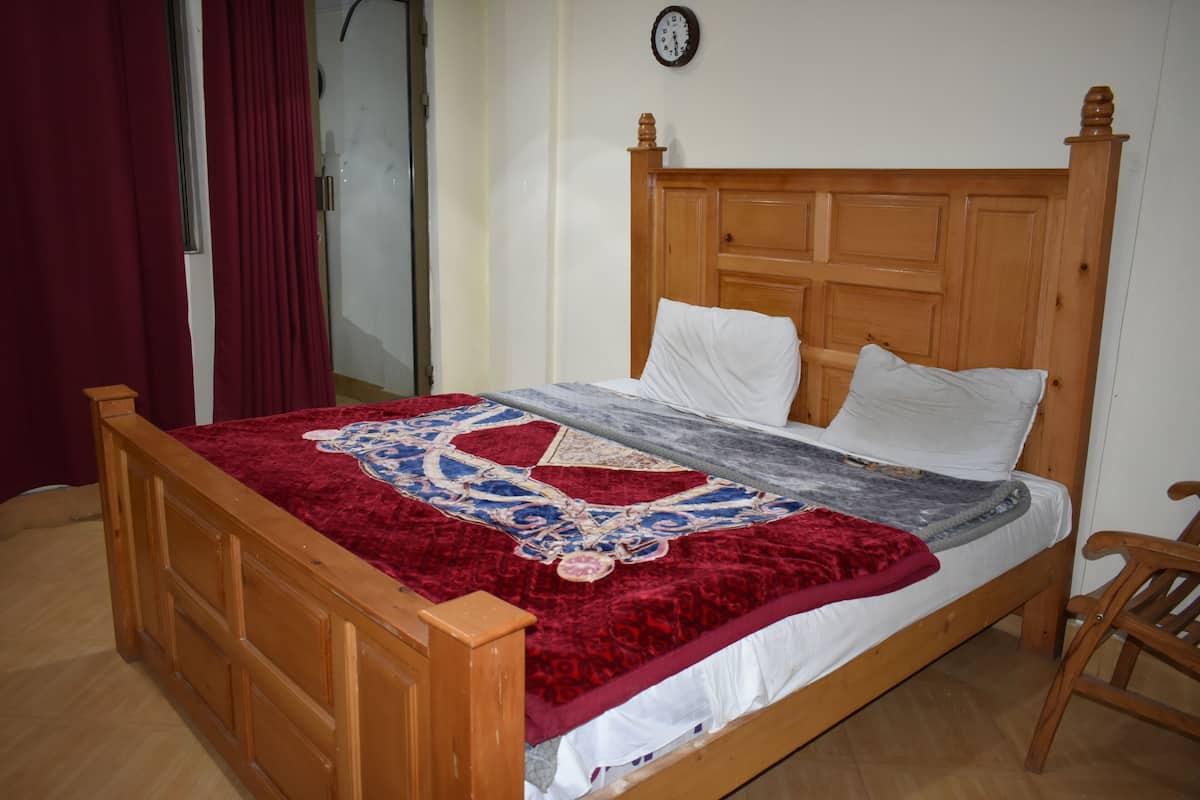 Un lit en bois avec une couvre-lit à motifs rouges et bleus, un oreiller blanc et une tête de lit en bois.