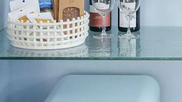 A kitchen counter with a white basket containing chocolate bars, a bag of coffee, and two wine glasses. Below, there is a light blue Smeg refrigerator.