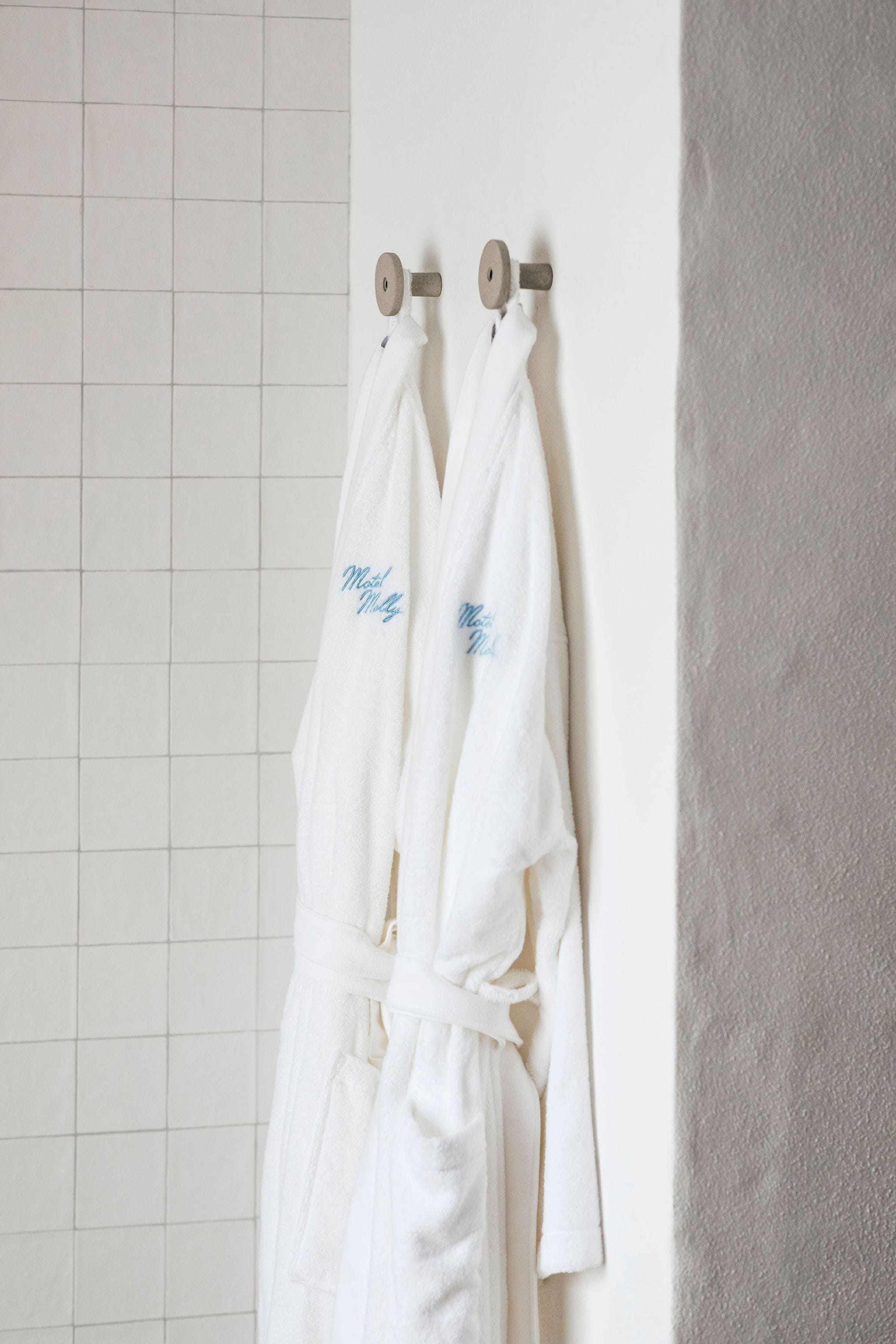 Dos albornoces blancos colgados en una pared con un diseño de cuadrícula.