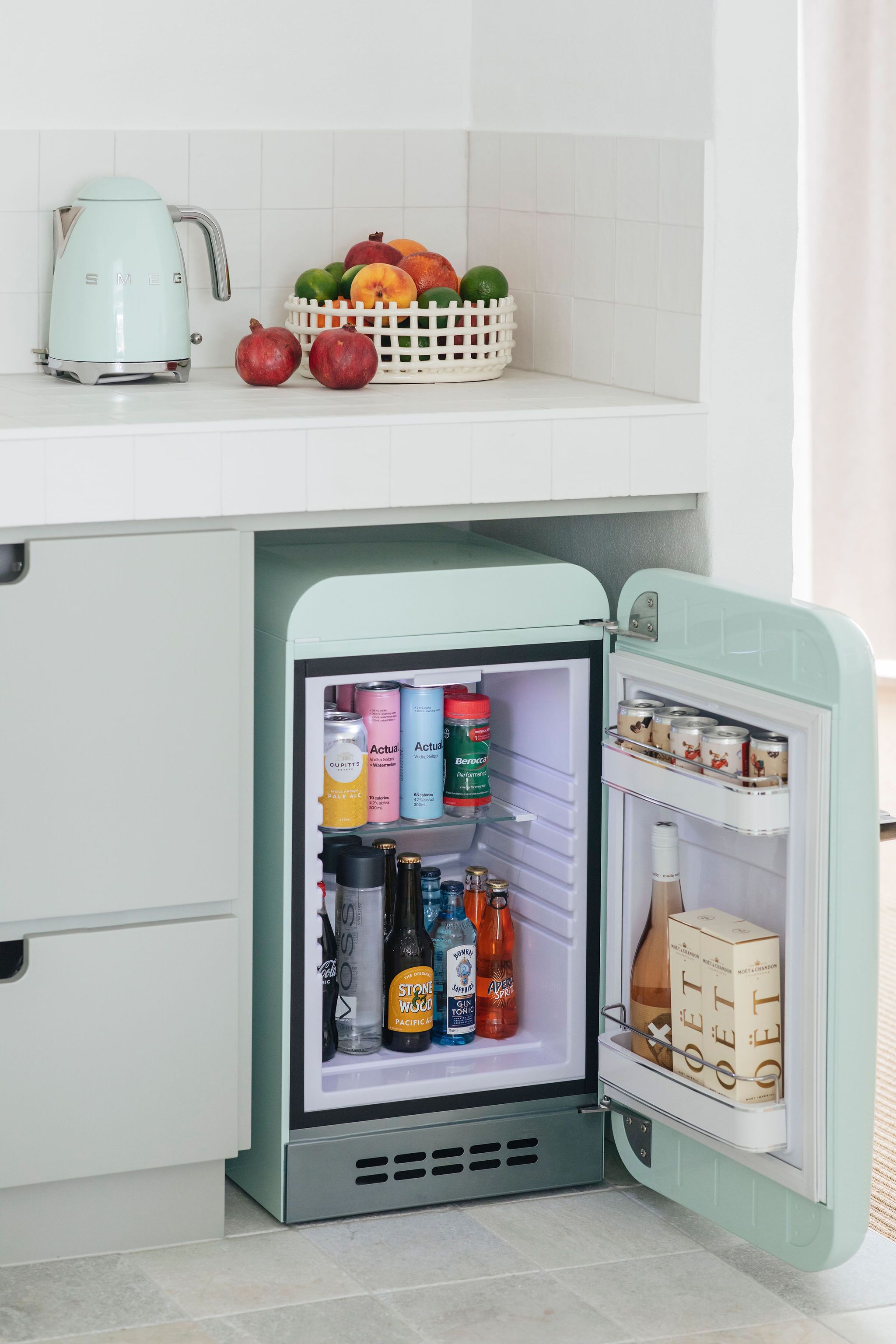 A retro-style refrigerator with a teal exterior, stocked with beverages, canned goods, and a box of beer.