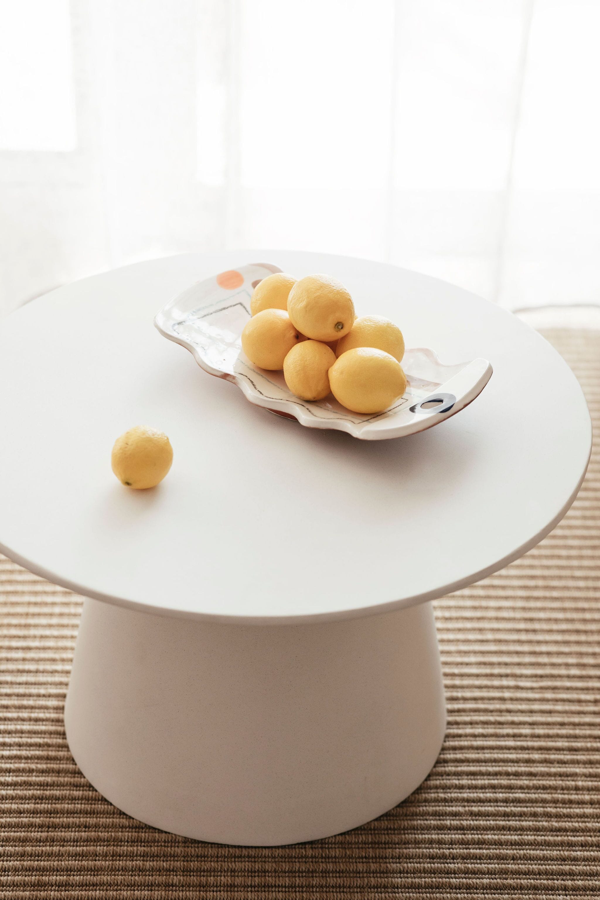 A white round table with a white plate holding several lemons.