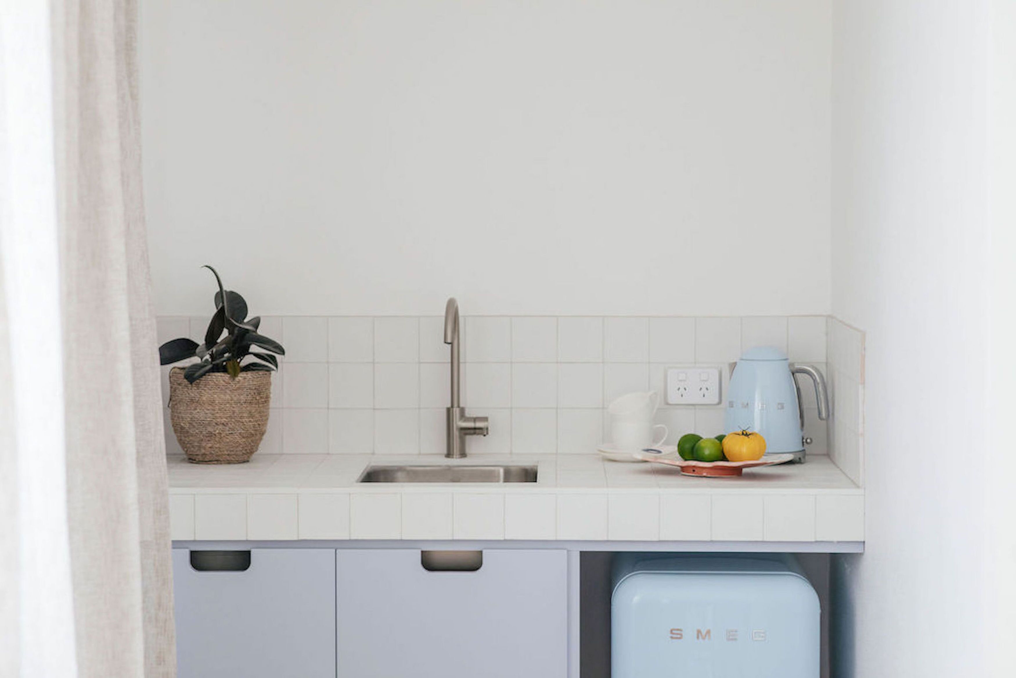 A kitchen with a white countertop, a sink, a kettle, and a dish rack with vegetables.
