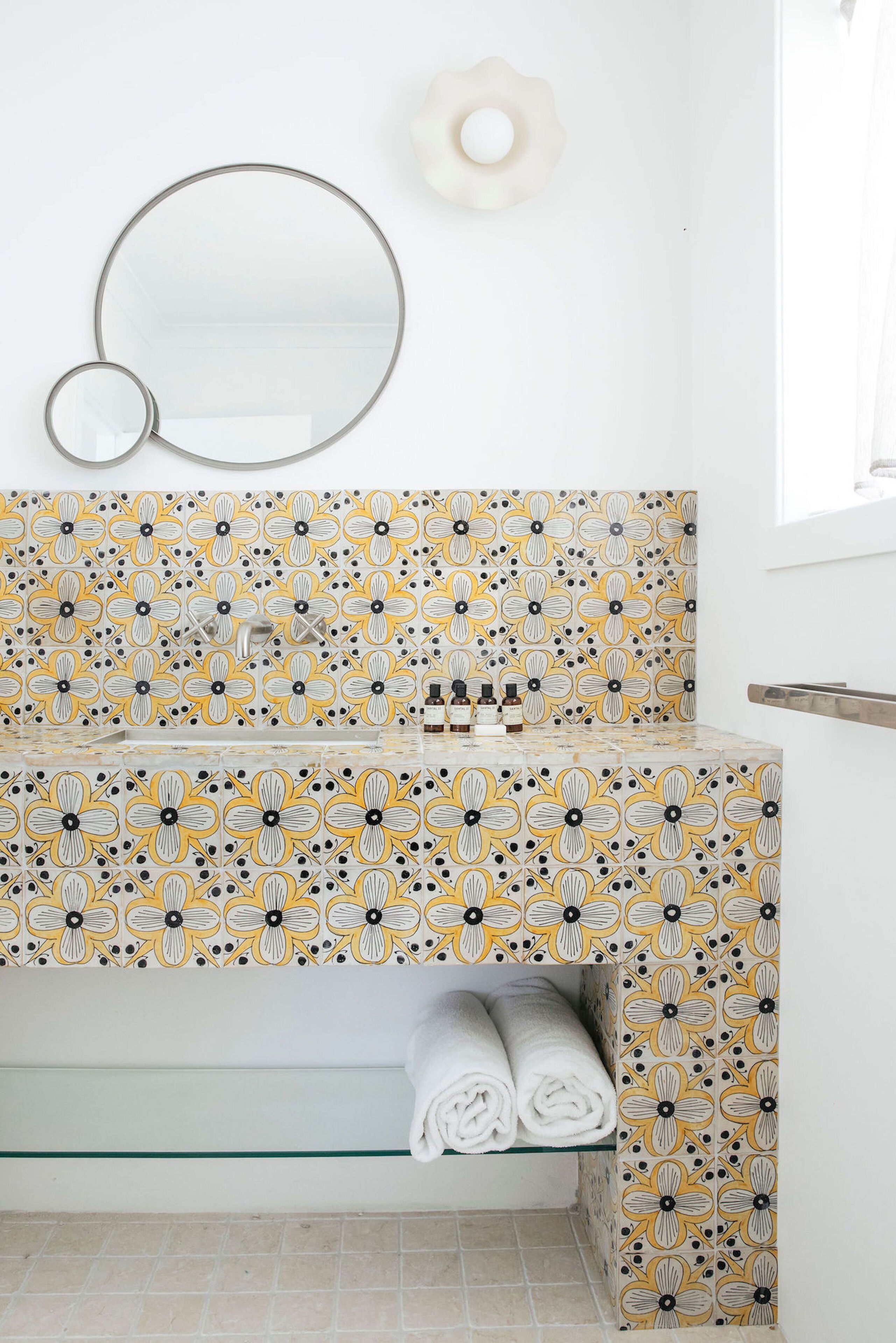A bathroom with a patterned tile backsplash, a mirror, a sink with toiletries, and a towel rack.