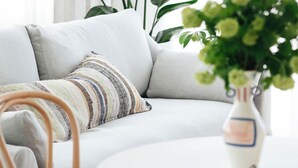 Una sala de estar moderna con un sofá gris, un cojín a rayas, una mesa redonda de madera y un jarrón con flores verdes.
