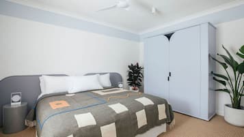A bedroom with a bed, a wardrobe, a ceiling fan, a bedside table, and a potted plant.