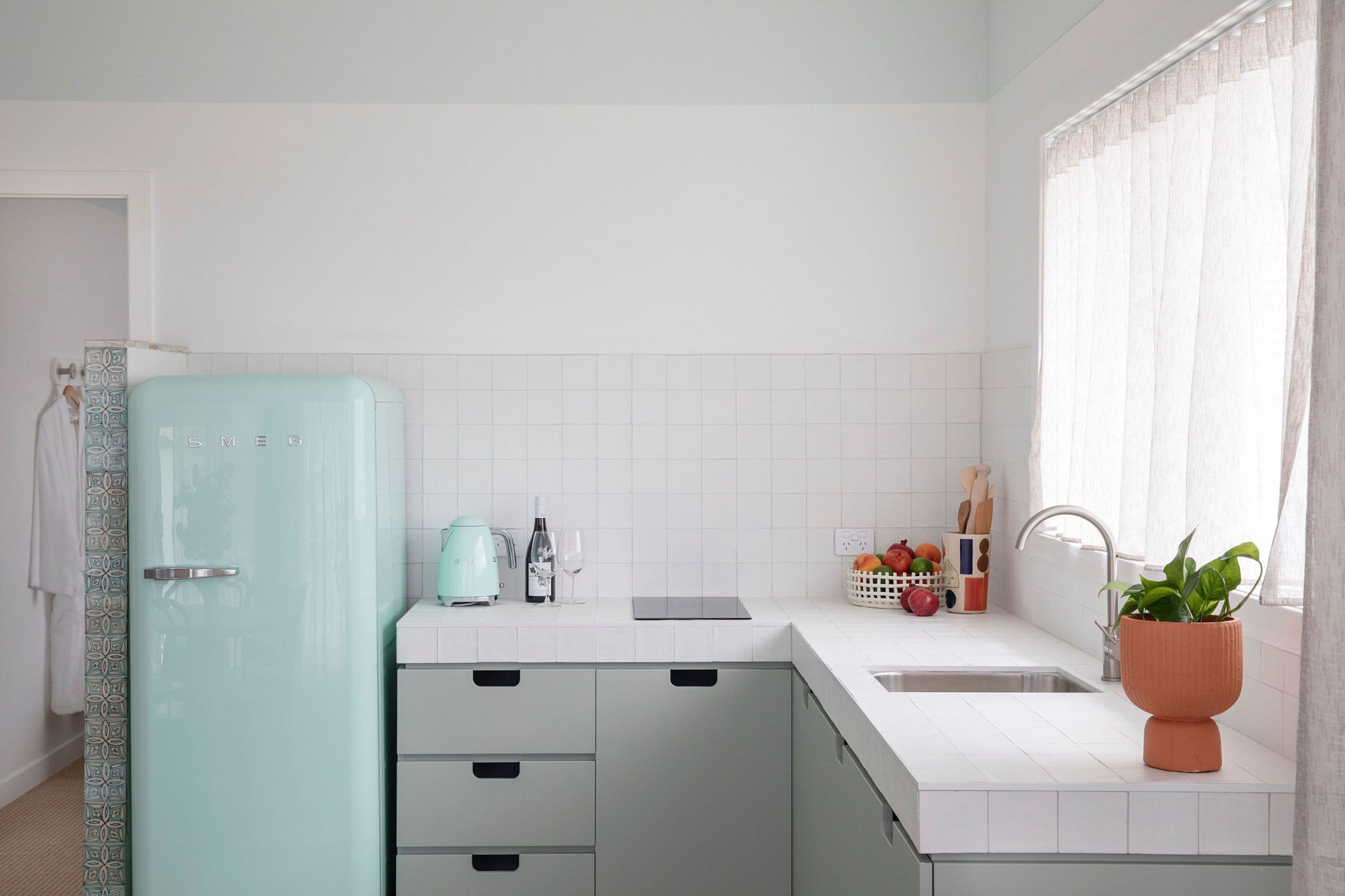 Una cocina moderna con un refrigerador verde menta, azulejos blancos, un lavabo y una planta en maceta.