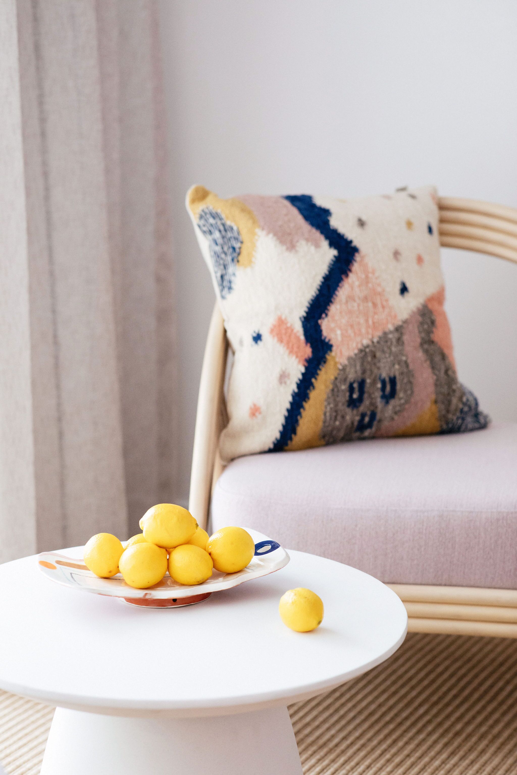 A white round table with a plate of lemons and a single lemon on it, placed on a beige floor.