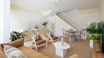A modern living room with a sofa, chairs, a coffee table, and a dining area with a table and chairs. There is a staircase leading to another level.
