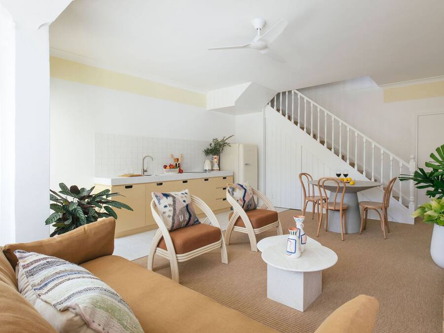 A modern living room with a sofa, chairs, a coffee table, and a dining area with a table and chairs. There is a staircase leading to another level.
