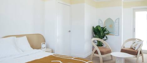 A hotel room with a bed, a small table, two chairs, a potted plant, and a door.