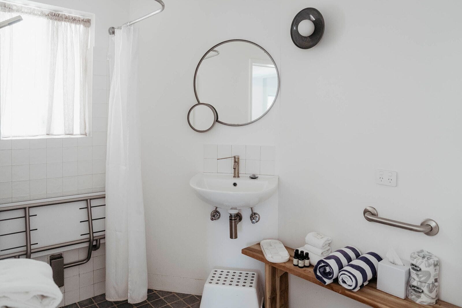 A bathroom with a white sink, a mirror, a towel rack, and a shelf with toiletries.