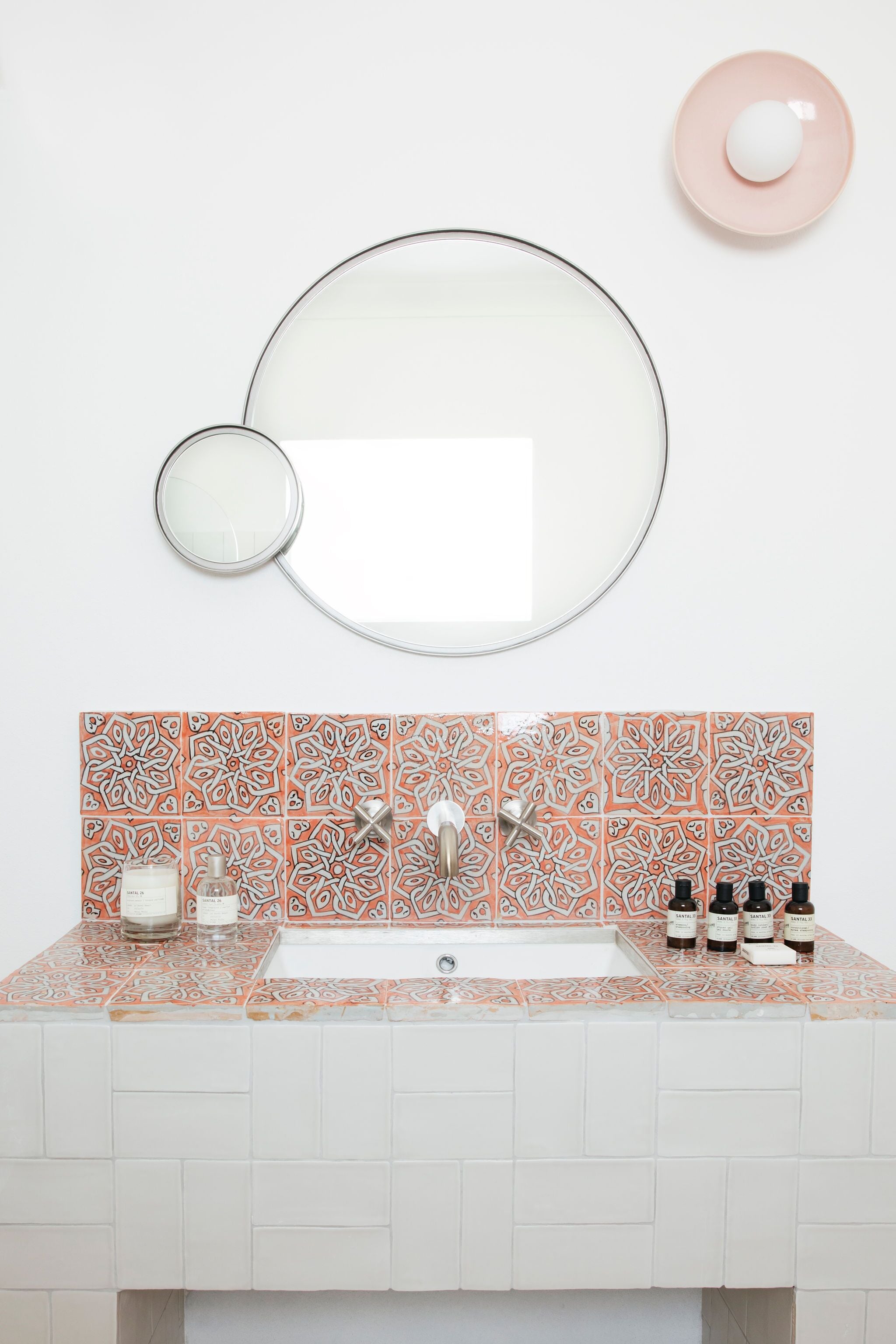 A bathroom with a sink, two faucets, a mirror, and a patterned tile backsplash.